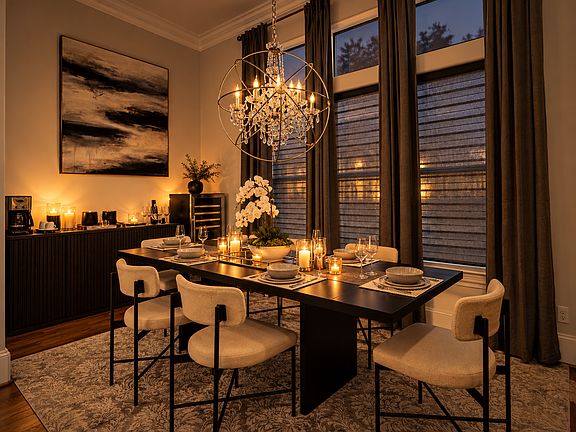 Elegant dining area with seating for six, a statement chandelier, floor-to-ceiling drapery, custom window shades, and a dedicated coffee and wine bar. Perfect for everyday dining and entertaining.