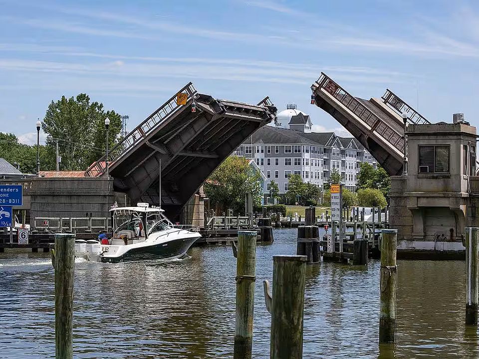 As a small boat enters the Deep Harbour Marina, the raised decks of the Cambridge Creek Draw Bridge frame "Cattail Cove."