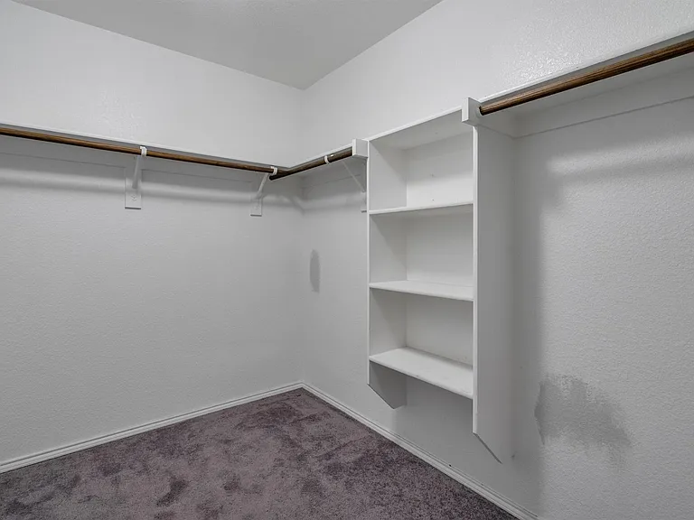 Walk-in closet featuring built-in shelving, two clothing rods, white walls, and gray carpet