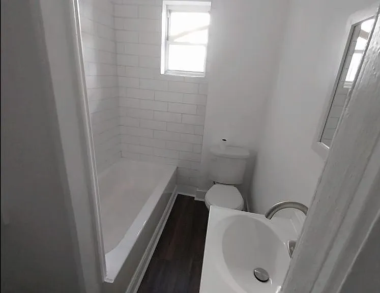 Efficient full bath featuring a shower combo, white tile surround, vanity sink, and a window for natural light.