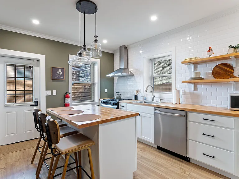 Updated kitchen with butcher-block island seating, stainless appliances, open shelving, and a deep sink by the window.