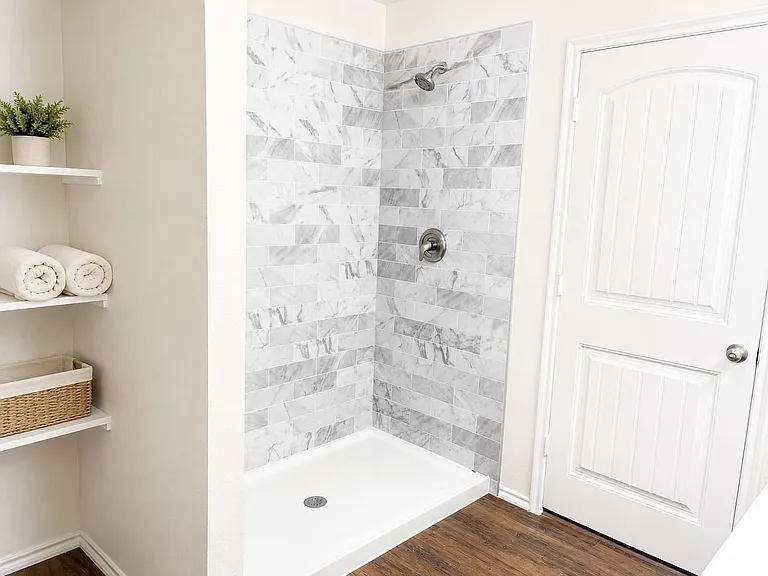 Shower enclosure featuring marble-patterned tile, a white shower pan, and chrome fixtures