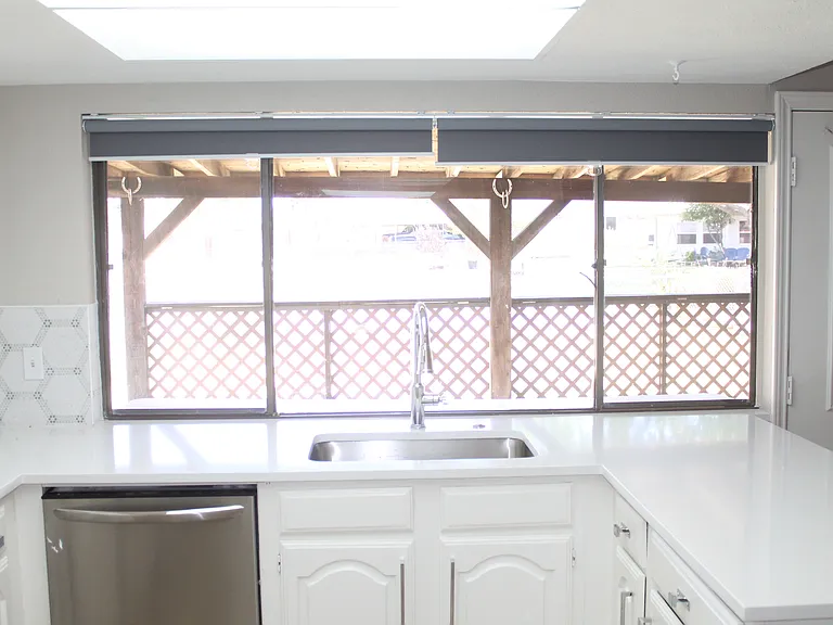 Extra-large window featuring roll-down shades for added privacy. Complete with stainless steel sink, oversized faucet, garbage disposal, and plenty of cabinetry.