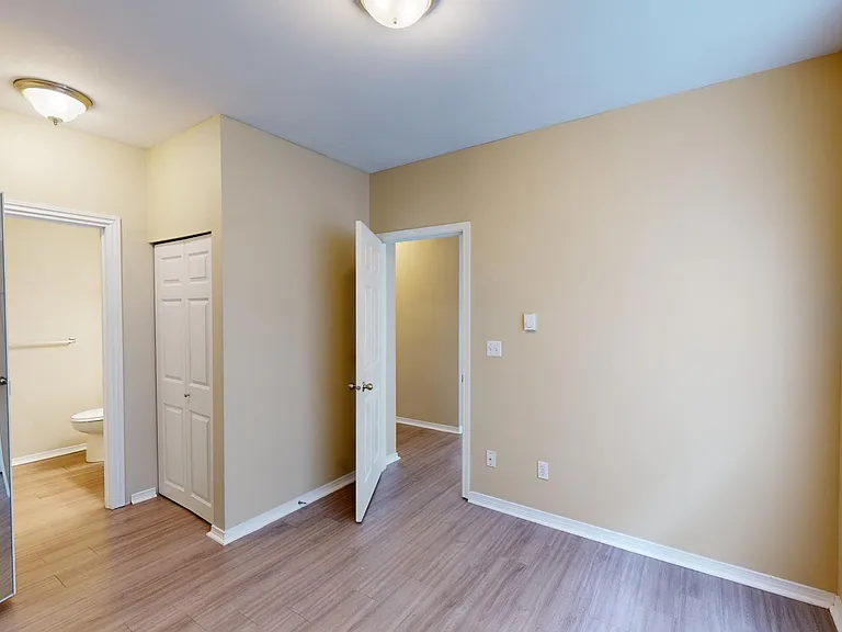 Spacious apartment bedroom with attached bathroom and wood-style flooring.