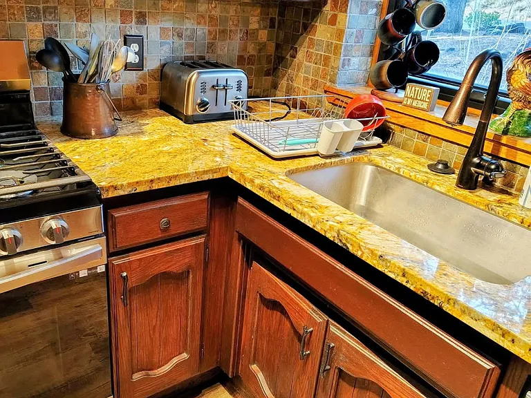 Efficient kitchen workspace with granite countertops, tile backsplash, ample wood cabinetry, and a window-side sink.