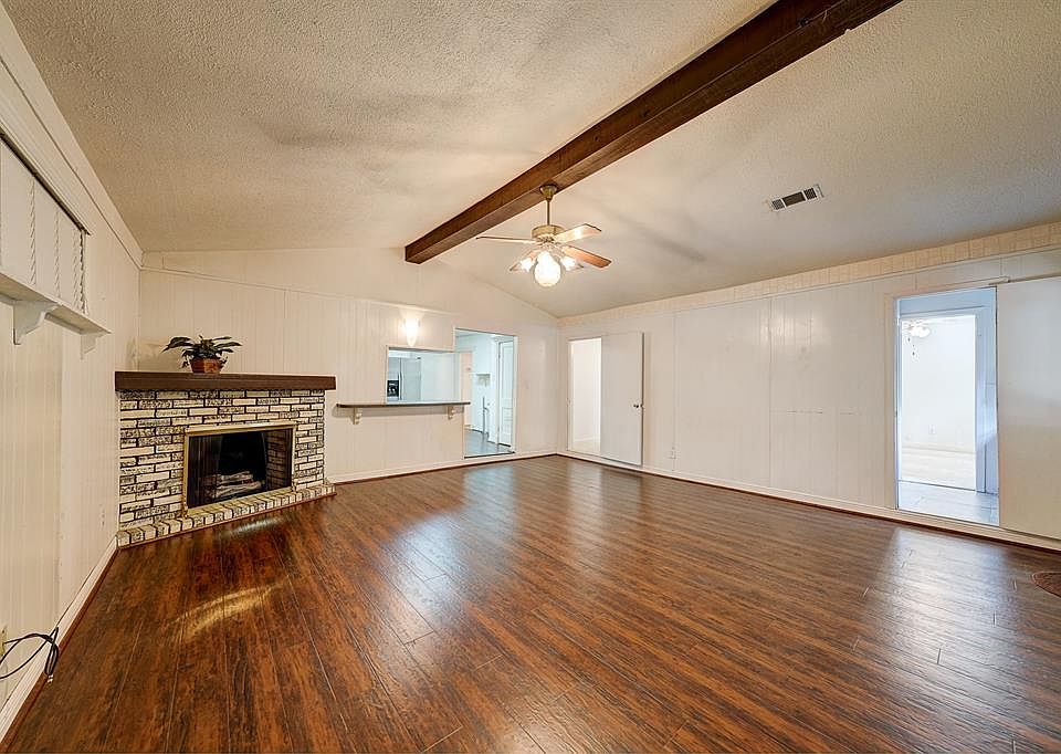 The 19âx19â den with a view of the vaulted, beamed ceiling, gas log fireplace, and kitchen beyond. The two doors on the right lead to the master bedroom and the en suite master bath.