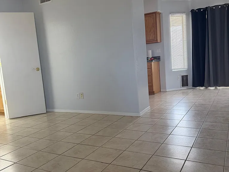 Walking into the unit, one can see the sliding patio door with Sun Blocking Drapes. A Galley kitchen is to the left, indicated by brown cabinets, while the half bath door is visible on the left side of the photo.