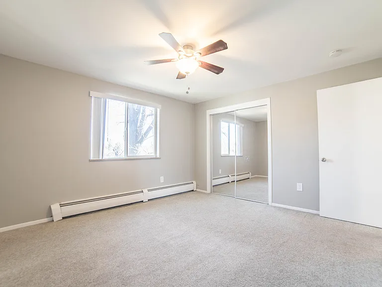 Bright and airy bedroom featuring plush carpeting, large window with natural light, and a mirrored closet for added elegance.