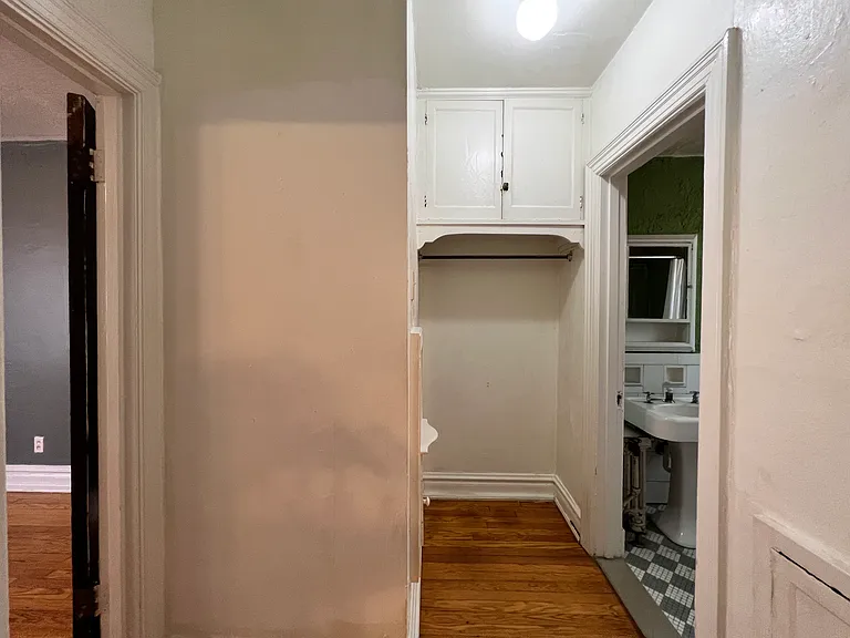 Back through the main living space, a doorway opens into this dressing area and then splits to the bathroom or bedroom. Above the closet rod, there is an upper cabinet for additional storage.