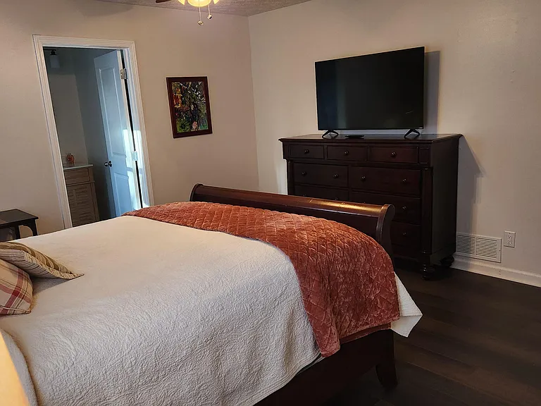 Furnished bedroom with a queen bed, dresser with TV, and easy access to an adjacent bathroom for added convenience.