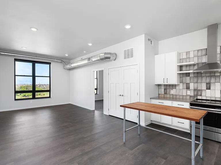 Modern open-concept apartment with sleek dark flooring, stylish kitchen, and large window offering scenic views. Modern open-concept apartment with sleek dark flooring, stylish kitchen, and large window offering scenic views.