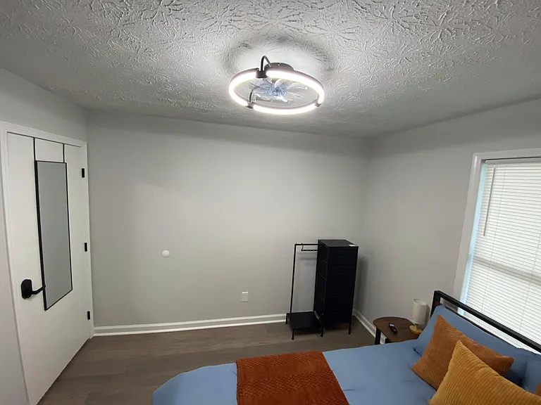 Bedroom offers a comfortable layout with a large window for natural light, overhead fan/light, and space for a dresser.