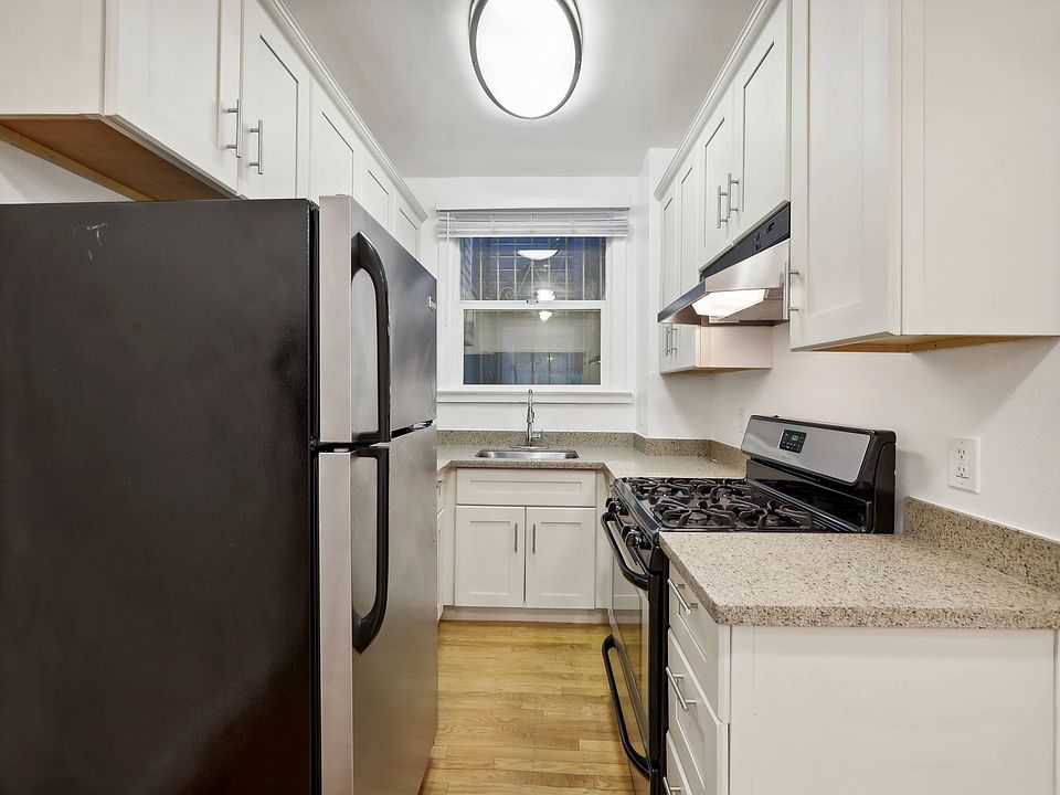 Kitchen with multiple cabinets, refrigerator, stove, range hood, and sink