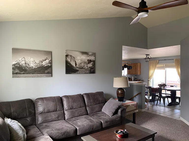 Open living area with sectional seating, ceiling fan, and a pass-through to the dining/kitchen space with patio access.