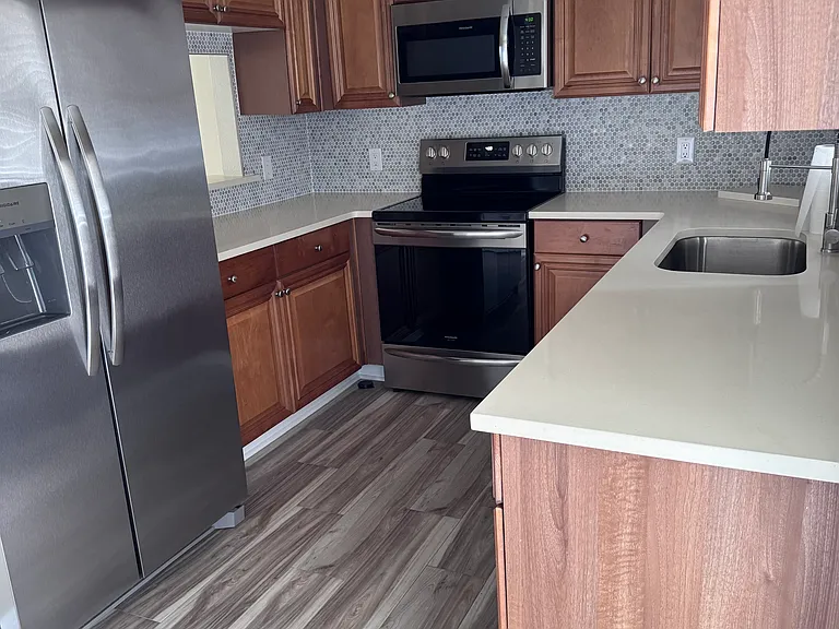 Kitchen with pass through window featuring quartz counters, custom backsplash, & stainless steel appliances.