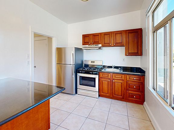 Kitchen with multiple cabinets, refrigerator, stove, range hood, and sink