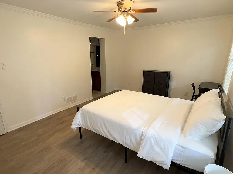 Spacious bedroom featuring wood-look flooring, ceiling fan with light, and a work desk, with convenient access to a vanity ar