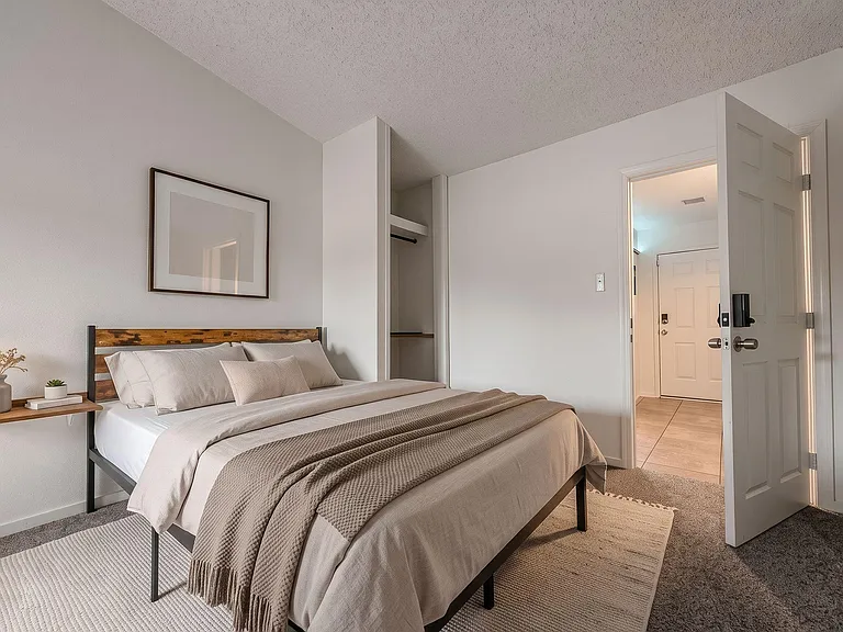 Furnished bedroom with a full bed, wall-mounted bedside shelf, and open closet storage for easy organization.