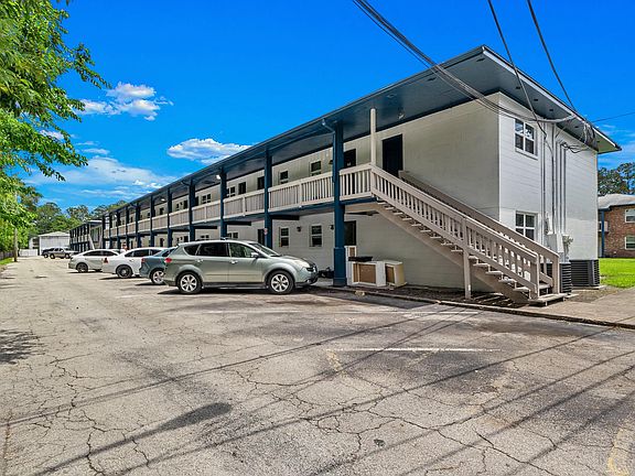 Charming two-story apartment complex with blue accents, ample parking, and a welcoming outdoor staircase under a clear blue sky.