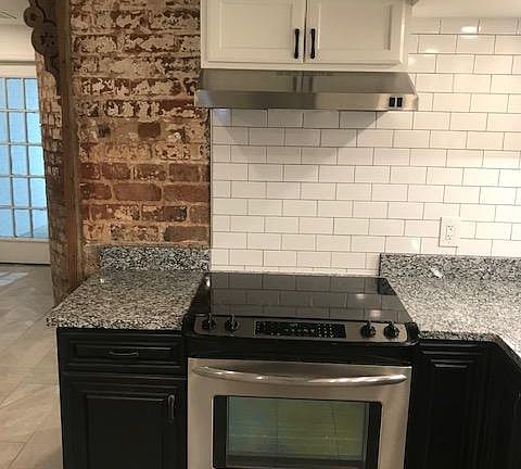 Stainless stove with Granite Counter top and exposed brick.