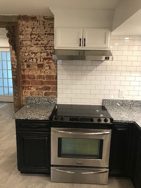 Stainless stove with Granite Counter top and exposed brick.