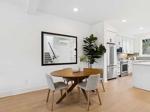 A modern, minimalist kitchen and dining area with a round wooden table, gray chairs, and a large pot