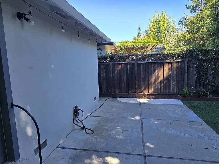 Private backyard completely fenced in with bistro lights and faux lawn.