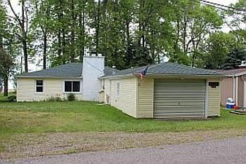 A view from the one way blacktop drive shows the cottage with the 1 car attached garage.