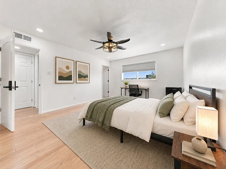 Spacious bedroom with wood-look floors, ceiling fan, a work desk by the window, and ample room for a full bed setup.