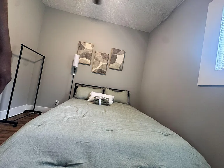 Furnished bedroom with a full-size bed, neutral finishes, and a window with blinds for natural light and privacy.