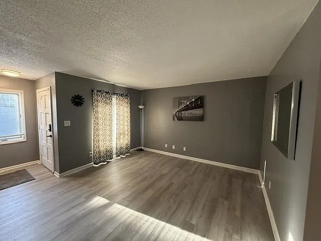 Open living area with wood-look flooring, gray walls, and a large window with patterned curtains for comfortable seating.