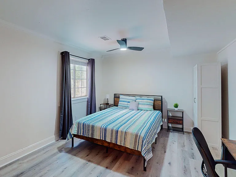 Furnished bedroom with a queen bed, nightstands, ceiling fan, and a large window with curtains for comfortable living.