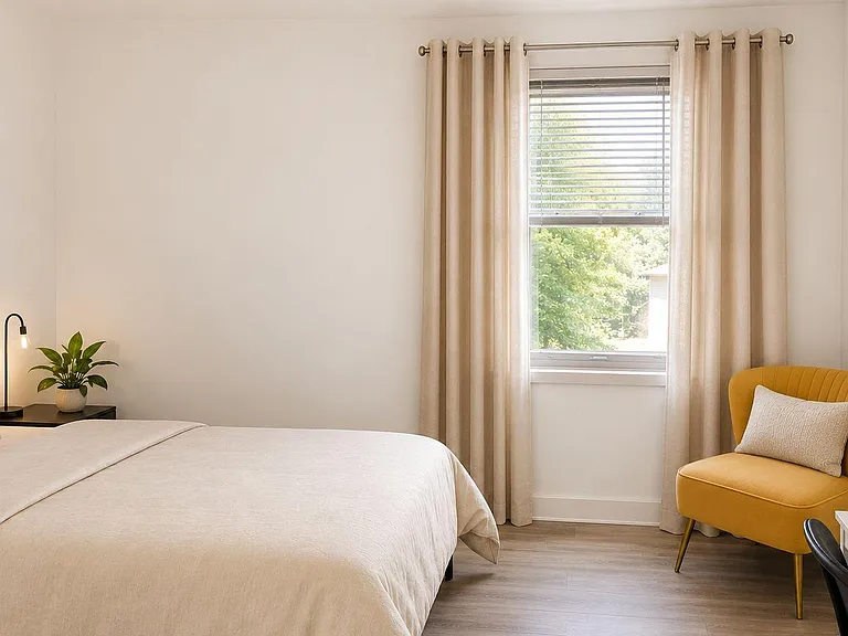 Well-appointed bedroom with a large window, full bed, bedside table with lamp, and a desk nook plus accent chair.