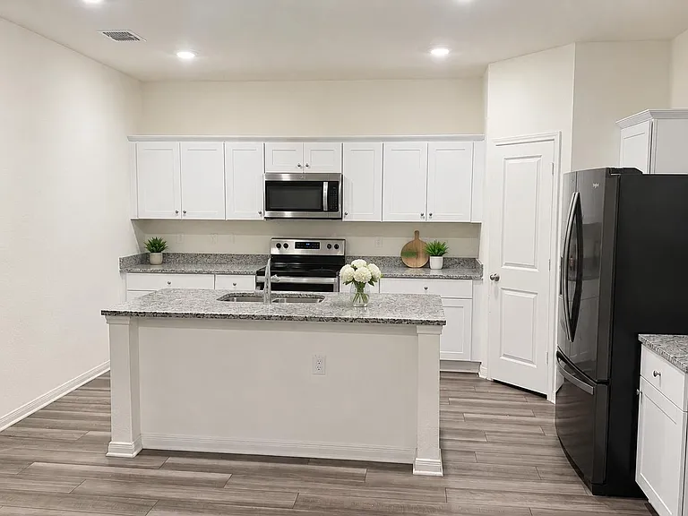 Open kitchen with large prep island, ample white cabinetry, stone-look counters, and stainless appliances plus pantry.