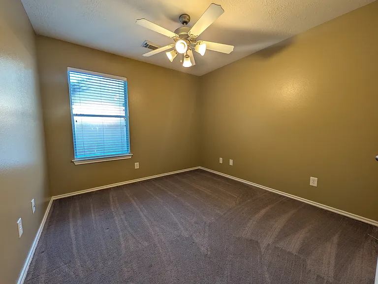 Another versatile bedroom space featuring a large window, comforting ceiling fan, and carpeted floors_perfect for guests or a home office.
