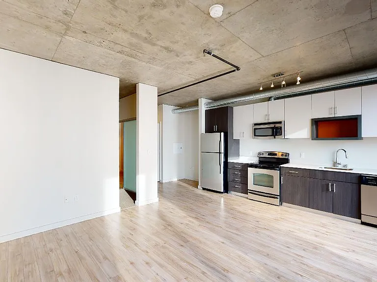 Apartment kitchen with stainless steel appliances, dining and living room with wood-style flooring.
