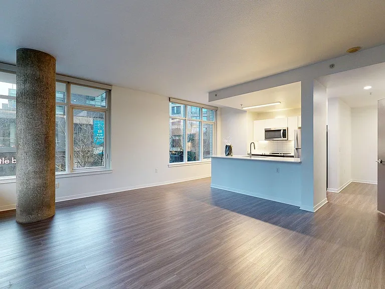 Apartment kitchen with stainless steel appliances, dining and living room with wood-style flooring.