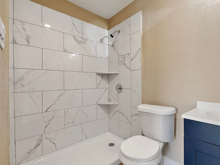 Full bath with a textured wall, tiled shower, and vanity
