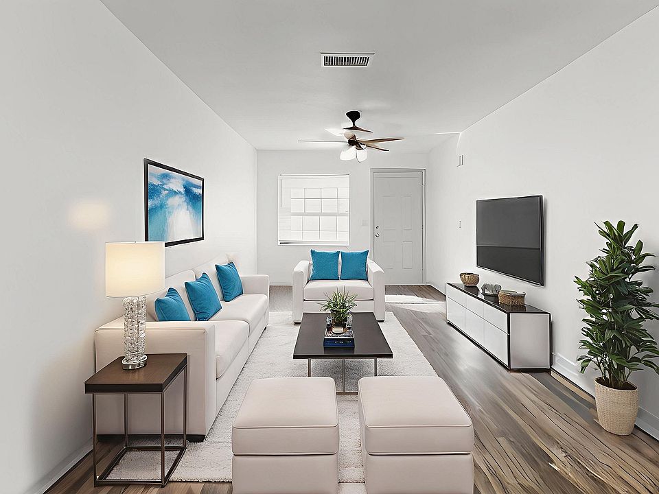 Bright and inviting living room with sleek modern decor, featuring white sofas, blue accent pillows, and a stylish coffee table. A flat-screen TV is mounted on the wall, complimented by elegant hardwood flooring and lush green plant for a touch of nature.