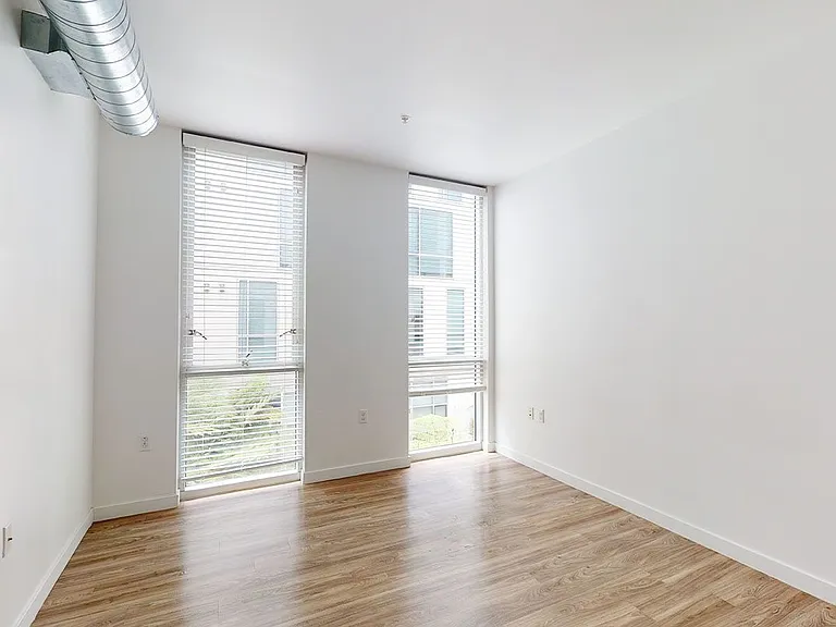 Spacious apartment bedroom with wood-style flooring and floor-to-ceiling windows.