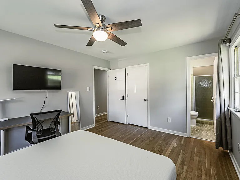 Private bedroom with hardwood floors, ceiling fan, mounted TV, and a dedicated desk area, plus convenient access to a nearby