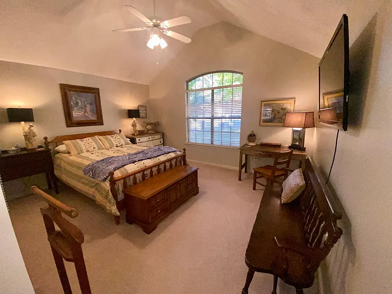 Vaulted guest room with queen bed and desk, plus wall mounted TV using a connected streaming service.