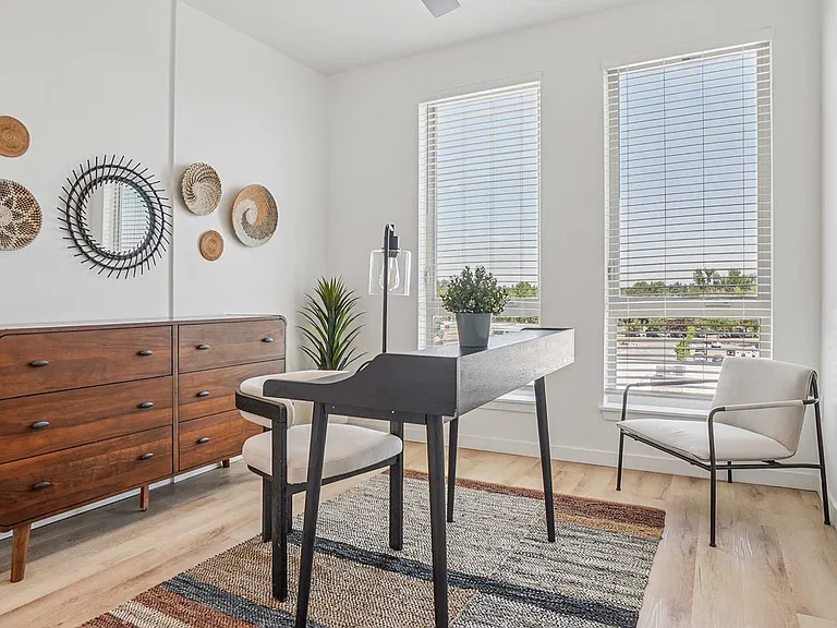 Create your ideal work-from-home setup in a bright, versatile room with oversized windows, modern furnishings, and warm wood-inspired finishes.