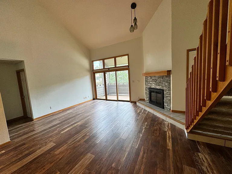 Open main living area with vaulted volume, fireplace, updated flooring, and direct access to the private deck.