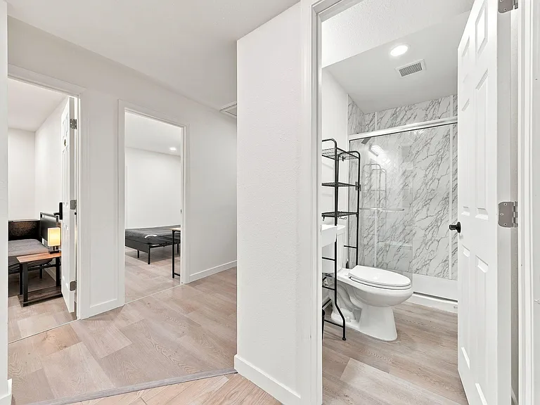 Full bathroom with tub/shower combo, marble-look surround, and storage shelving off the hallway near bedrooms.