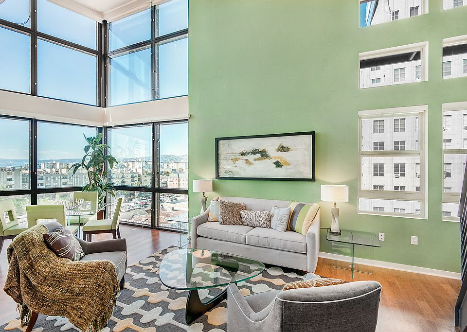 Staged living room with hardwood-style flooring, high ceilings and floor to ceiling windows.