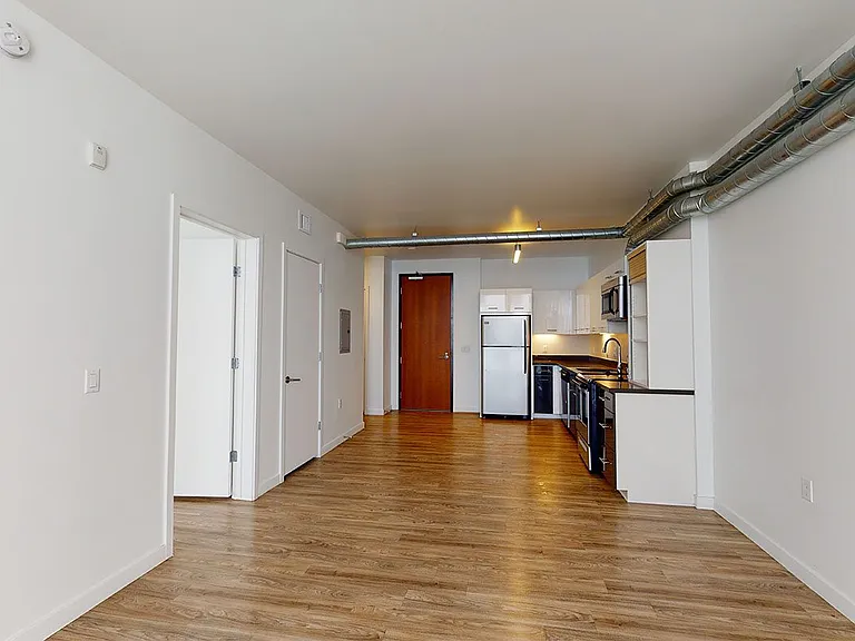 Apartment kitchen with stainless steel appliances, dining and living room with wood-style flooring and floor-to-ceiling windows.