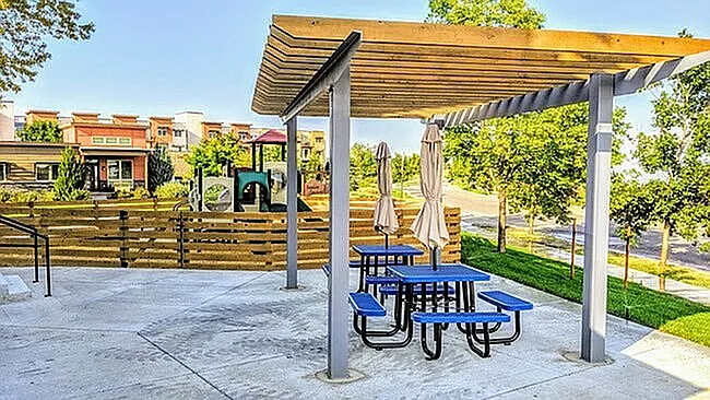 Charming outdoor space with a modern pergola, picnic tables, and vibrant greenery, perfect for relaxation in a friendly community setting.
