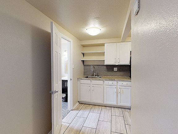 Inviting kitchen with sleek white cabinets and modern mosaic backsplash, leading to a well-lit bathroom area.