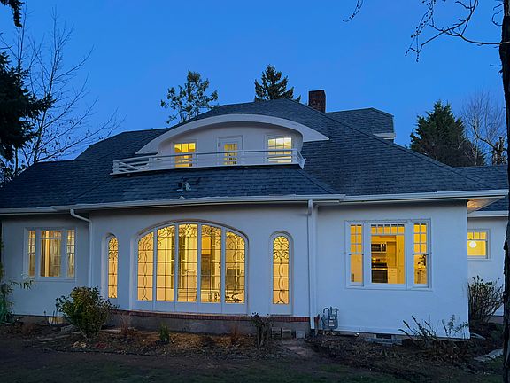 An evening view of the side yard. The yard features a cedar fence for privacy and an inviting balance of sun and shade, with three Douglas Firs and a maple. This photo highlights the main level sunroom and upstairs apartment balcony.